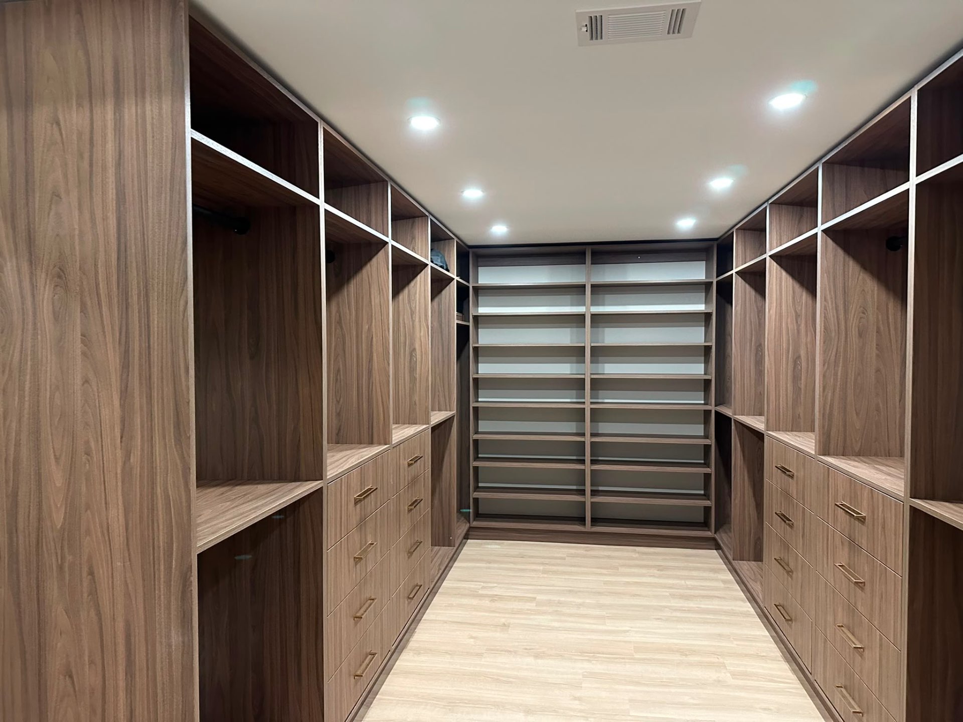 Finished walnut walk-in primary closet with brass pulls
