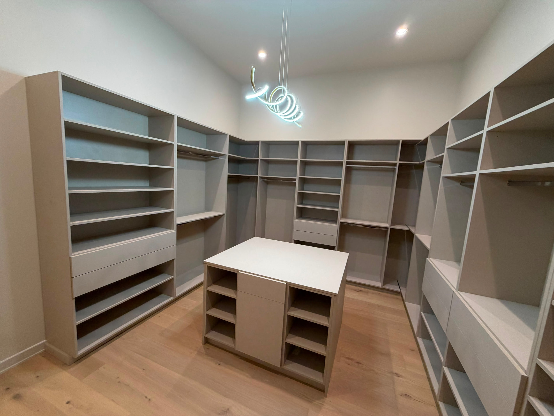 Custom walk-in primary closet with floor-to-ceiling cabinetry, center island and sculptural LED chandelier