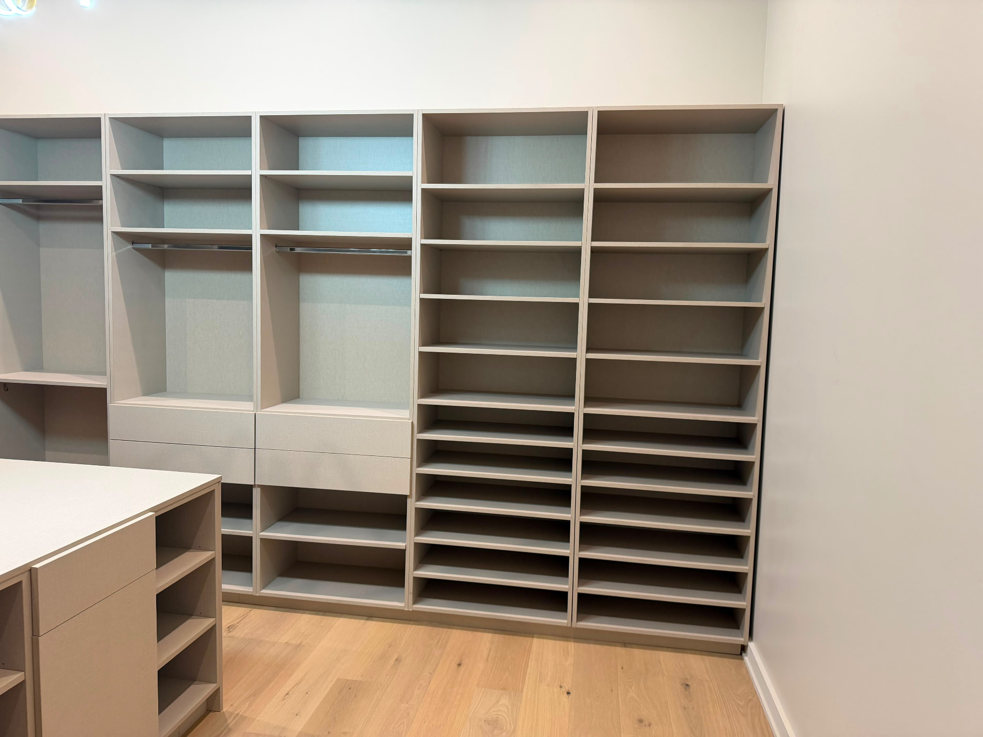 Custom closet display shelving with hanging rods and deep drawers in warm greige finish