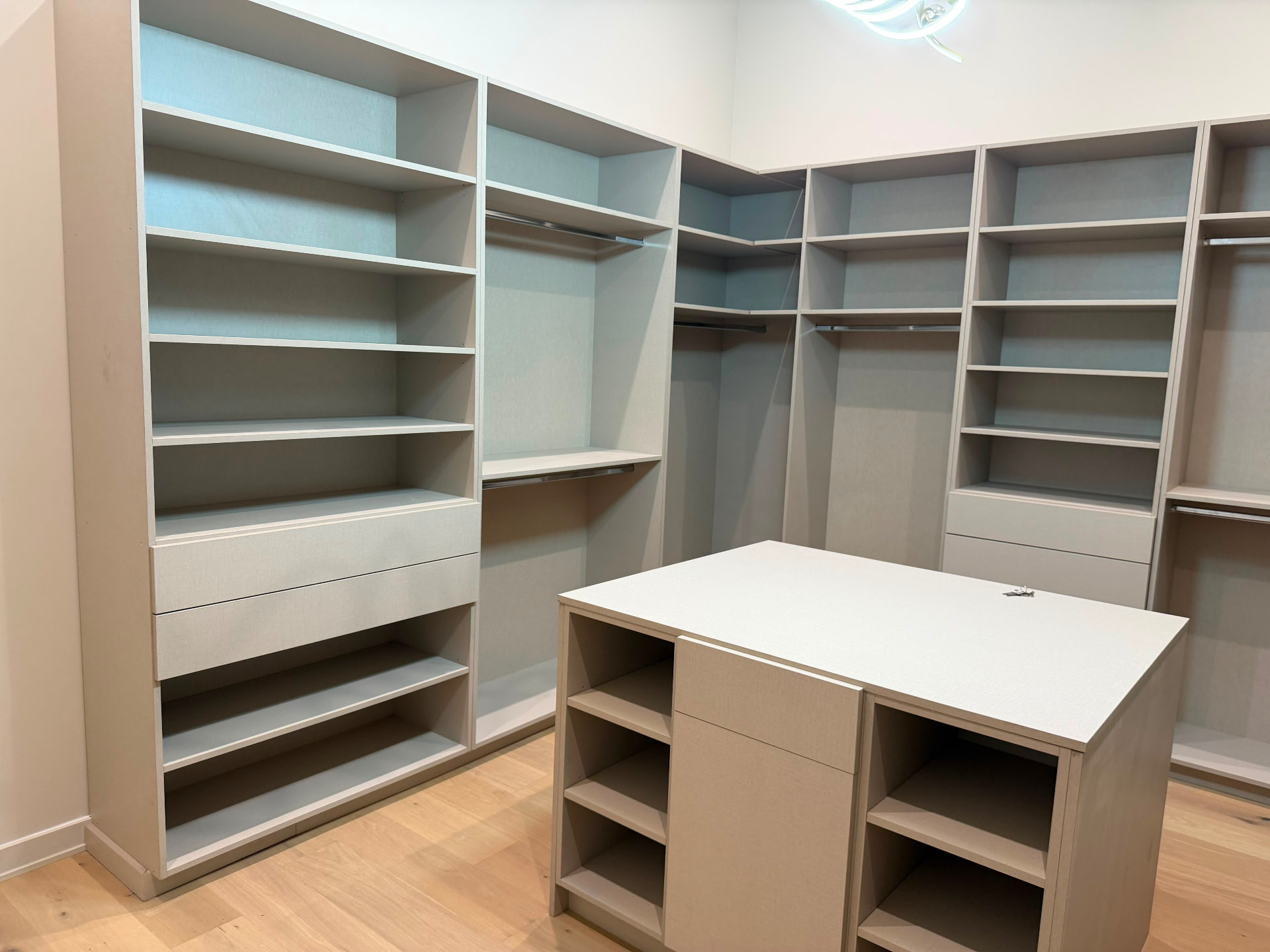Walk-in closet with quartz-top island, drawer banks and open shelving on white oak flooring