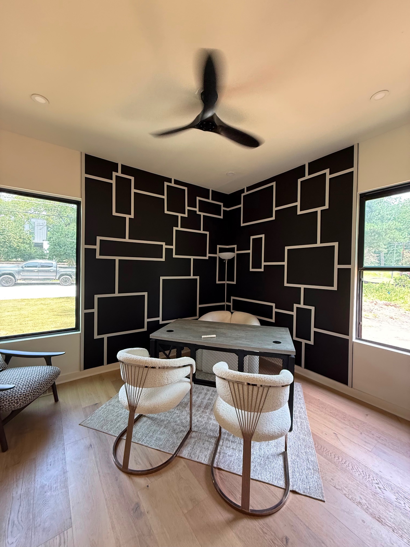 Modern home office with black square-grid paneled accent wall and bouclé lounge chairs